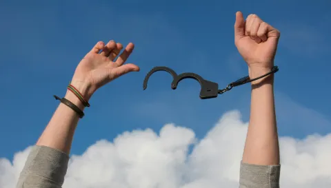 Braços erguidos ao céu com uma algema aberta, simbolizando liberdade, superação e resiliência diante das adversidades.